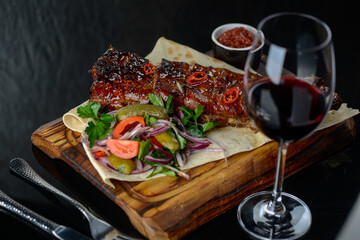 fried ribs on pita bread with salad on a black background with a glass of wine

