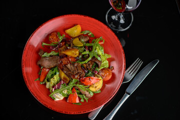 warm salad with veal in a red plate on a dark background

