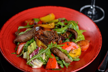 warm salad with veal in a red plate on a dark background macro photo
