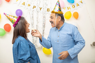 Happy Indian asian middle age couple celebrate birthday together eating cake and party at home. 