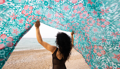 A woman holds a headscarf over her head and the wind blows her shawl