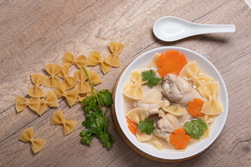 Macaroni soup with chicken thighs in clear broth with carrots.on an rustic old wood background.