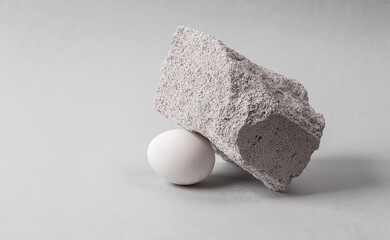 Minimalistic scene of a white chicken egg under a large heavy stone. Business concept