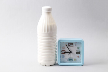 Plastic bottle of milk and clock on gray background