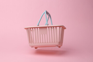 Supermarket basket flying in antigravity on pink background with shadow. Levitation object in the...