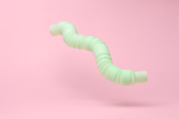 Antistress sensory pop tube toy flying in antigravity on pink background with shadow. Pastel color trend. Levitation object in the air. Creative minimal layout