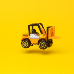 Miniature toy forklift flying in antigravity on yellow background with shadow. Levitation object in the air. Logistics, transportation concept. Creative minimal layout