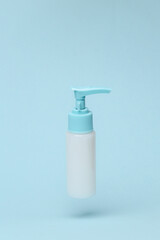 Cream dispenser bottle flying in antigravity on blue background with shadow. Levitation object in the air. Beauty and fashion concept. Creative minimal layout