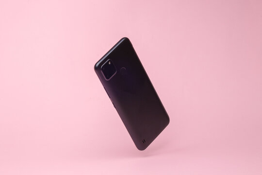 Modern Smartphone Backside With Camera Flying In Antigravity On Pink Background With Shadow. Levitation Object In The Air. Creative Minimal Layout