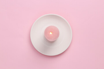 Flaming pink candle on a saucer, pink pastel background