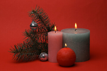 Flaming wax candles with fir branch and and Christmas decor on red background