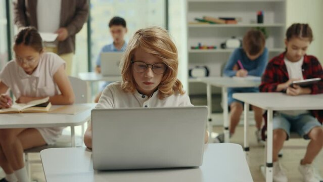 School boy using the computer sitting doing homework in the class during computer science lesson. People and technology concept. Elementary school class. Learning and education concept.