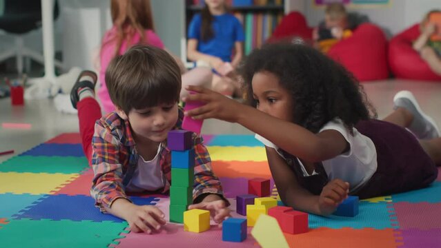 Cute multiethnic preschool kids playing with colored blocks on floor at nursery school