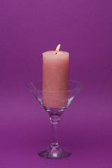 Minimalistic still life with a cocktail glass and a candle on a purple background