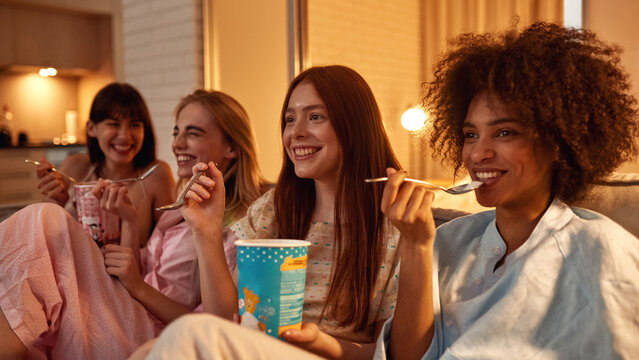 Laughing girls eat ice cream and watch TV or movie