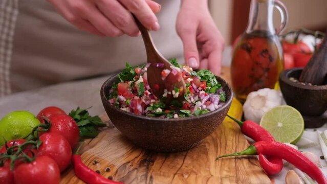 Slow motion shot of woman mixing salsa dip sauce ingredients in wooden bowl