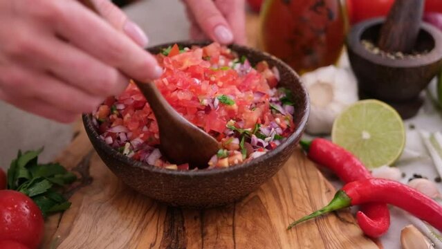 Slow motion shot of woman mixing salsa dip sauce ingredients in wooden bowl