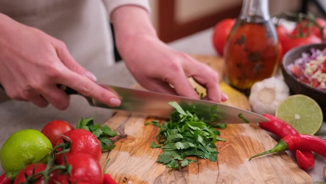 Woman cutting and chopping cilantro or parsley greens on a wooden board