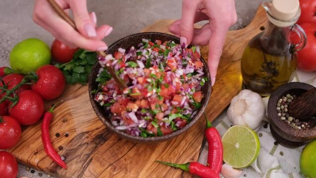 Slow motion shot of woman mixing salsa dip sauce ingredients in wooden bowl