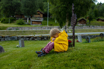 Sad little child, blond boy, standing in rain on cemetery, sad person, mourning