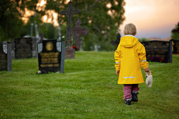 Sad little child, blond boy, standing in rain on cemetery, sad person, mourning