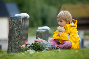 Sad little child, blond boy, standing in rain on cemetery, sad person, mourning