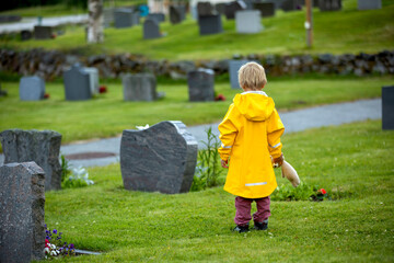 Sad little child, blond boy, standing in rain on cemetery, sad person, mourning