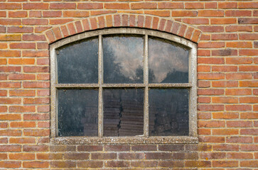 Old concrete window frame with a dirty reflective pane. The window is part of a Dutch barn.
