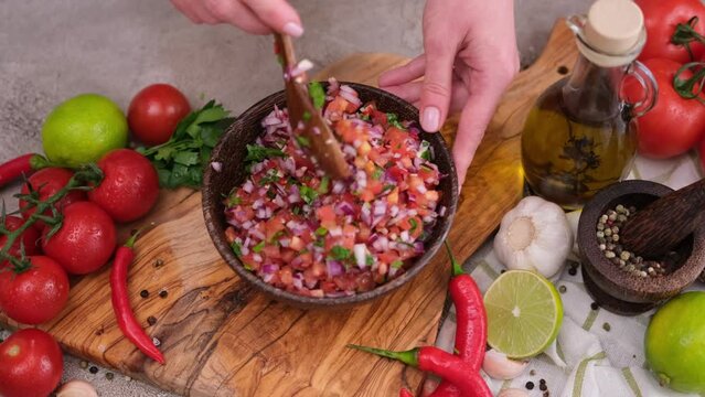 Slow motion shot of woman mixing salsa dip sauce ingredients in wooden bowl