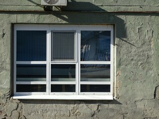 Full-color horizontal photo. A white window in the wall. Old plastered textured wall. Bright sunny day.