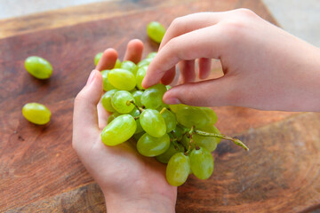 a woman's hand with green grapes, wooden background, concept of fresh sweet fruits and healthy food