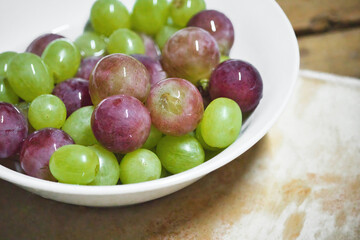 A white ceramic bowl full of green and purple or red unpeeled grapes