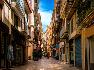 Street view of empty Carrer de l'Argenteria in a mediterranean shopping district of Palma de Mallorca with unrecognizable pedestrians, small businesses, coffee shops and restaurants on a summer day.