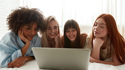 Young positive girlfriends watching laptop on bed