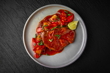 Beef or pork steak with stewed vegetables and sauce in a ceramic plate on a dark textured background. Restaurant menu Isolated on black