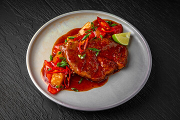 Beef or pork steak with stewed vegetables and sauce in a ceramic plate on a dark textured background. Restaurant menu Isolated on black