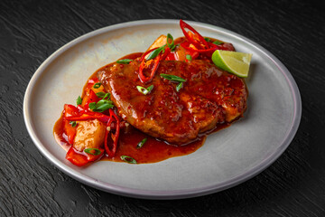 Beef or pork steak with stewed vegetables and sauce in a ceramic plate on a dark textured background. Restaurant menu Isolated on black