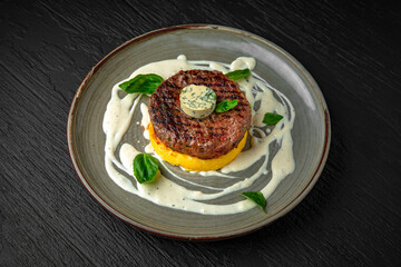 Beef steak or minced meat patty on a bed of mashed potatoes or sweet potatoes in a ceramic plate on a dark textured background. Restaurant menu Isolated on black