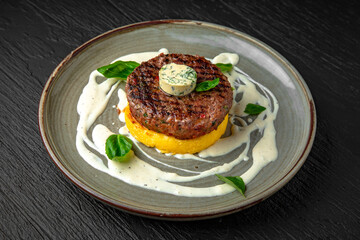 Beef steak or minced meat patty on a bed of mashed potatoes or sweet potatoes in a ceramic plate on a dark textured background. Restaurant menu Isolated on black