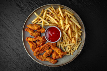 Chicken nuggets in batter, french fries and sauce. Fast food. Satiated nutritious food in a ceramic plate on a dark textured background. Restaurant menu Isolated on black