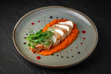 Chicken fillet with zucchini and carrot puree in a ceramic plate on a dark textured background. Restaurant menu Isolated on black