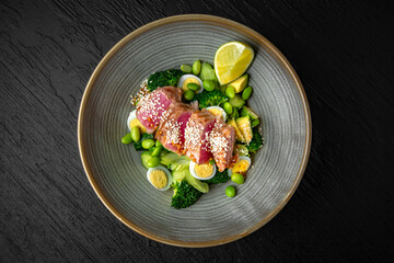 Salad with tuna, green beans, quail eggs, avocado in a ceramic plate on a dark textured background. Restaurant menu Isolated on black
