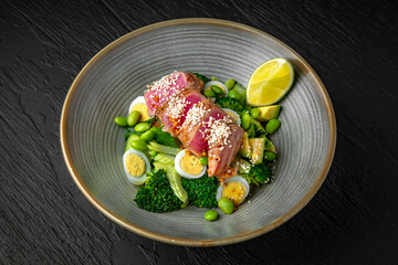 Salad with tuna, green beans, quail eggs, avocado in a ceramic plate on a dark textured background. Restaurant menu Isolated on black