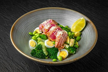 Salad with tuna, green beans, quail eggs, avocado in a ceramic plate on a dark textured background. Restaurant menu Isolated on black
