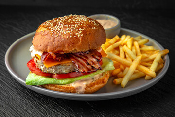 Delicious nutritious burger and fries. Fast food. Hearty food in a ceramic plate on a dark textured background. Restaurant menu Isolated on black
