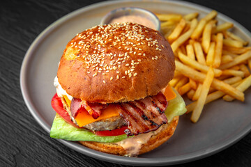 Delicious nutritious burger and fries. Fast food. Hearty food in a ceramic plate on a dark textured background. Restaurant menu Isolated on black