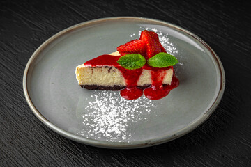 Dessert cheesecake with strawberries and mint in a ceramic plate on a dark textured background. Restaurant menu Isolated on black