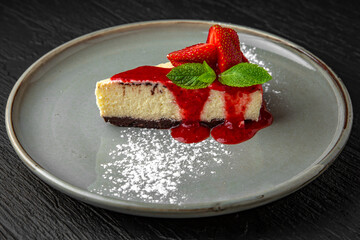 Dessert cheesecake with strawberries and mint in a ceramic plate on a dark textured background. Restaurant menu Isolated on black
