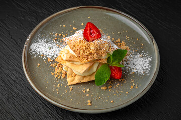 Napoleon dessert with delicate custard and strawberries in a ceramic plate on a dark textured background. Restaurant menu Isolated on black