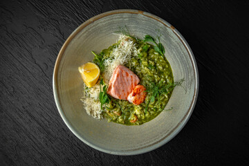 Risotto with spinach, avocado, salmon, shrimp and parmesan in a ceramic plate on a dark textured background. Restaurant menu Isolated on black